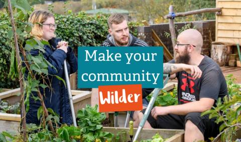 2 men and 1 woman in a community garden holding gardening equipment while talking to each other with the text 'Make your community wilder' across the photo