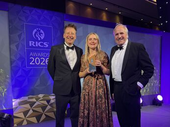 three people dressed smartly, standing on a stage, proudly holding their award trophy