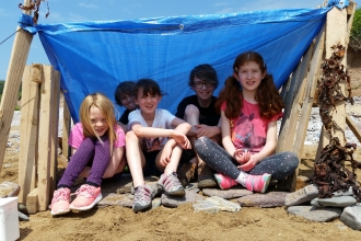 Children sitting under a makeshift shelter at Wembury beach