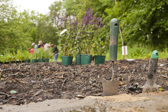 Gardening tools in the ground with flowers and a group of people in the distance