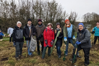 Group smiling at camera holding tools and trees