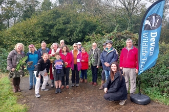 Group of people gathered together in front of hedge and devon wildlife trust banner, with boy holding up a wilder communities plaque