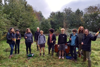 Group of young people gathered in woodland area, holding trowels and other tools