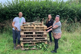 Emily NDN Officer and two residents from Grandisson Court standing next to a large bug hotel made of old wooden pallets