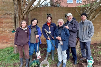 Group of people holding gardening equipment and smiling at the camera