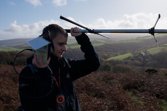 Young Jack Standing on top of hill on Exmoor Radio Tracking with receiver close to his ear