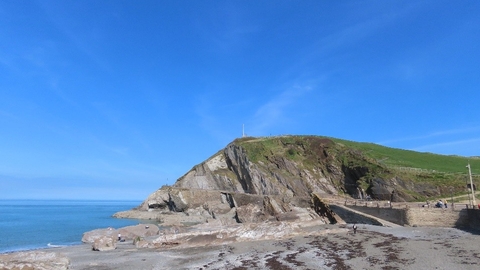 beach with a large rocky, hillside, blue sky behind