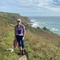 Maisie standing on a coast path with binoculars round neck and cap on