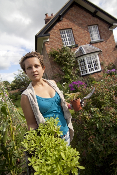 Gardening with wildlife, woman walking along with pack of plug plants, house and garden in background
