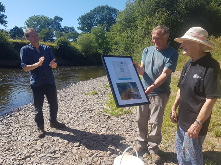 Diana Goodacre being presented a framed award by a trustee with DWT CEO Harry Barton next to river