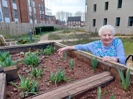 An elderly woman next to a flower bed