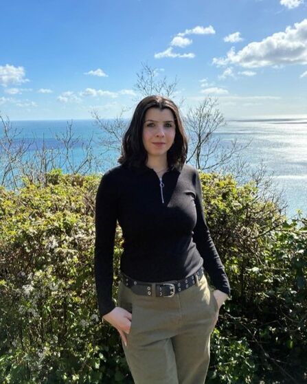 Photo of Wendy smiling slightly at the camera, with a view of the ocean behind