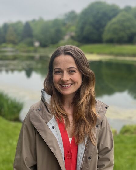 Head and shoulder shot of Anna smiling at the camera, with a large pond behind her