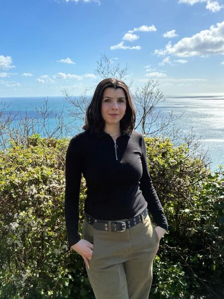 Photo of Abigail smiling slightly at the camera, with a view of the ocean behind
