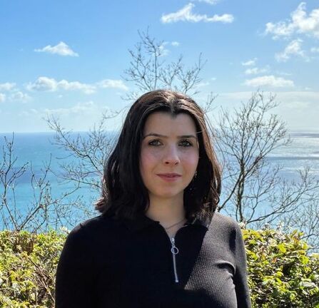 Photo of Abigail smiling slightly at the camera, with a view of the ocean behind
