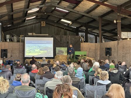 the backs of audience members sat listening to the presenter in a barn